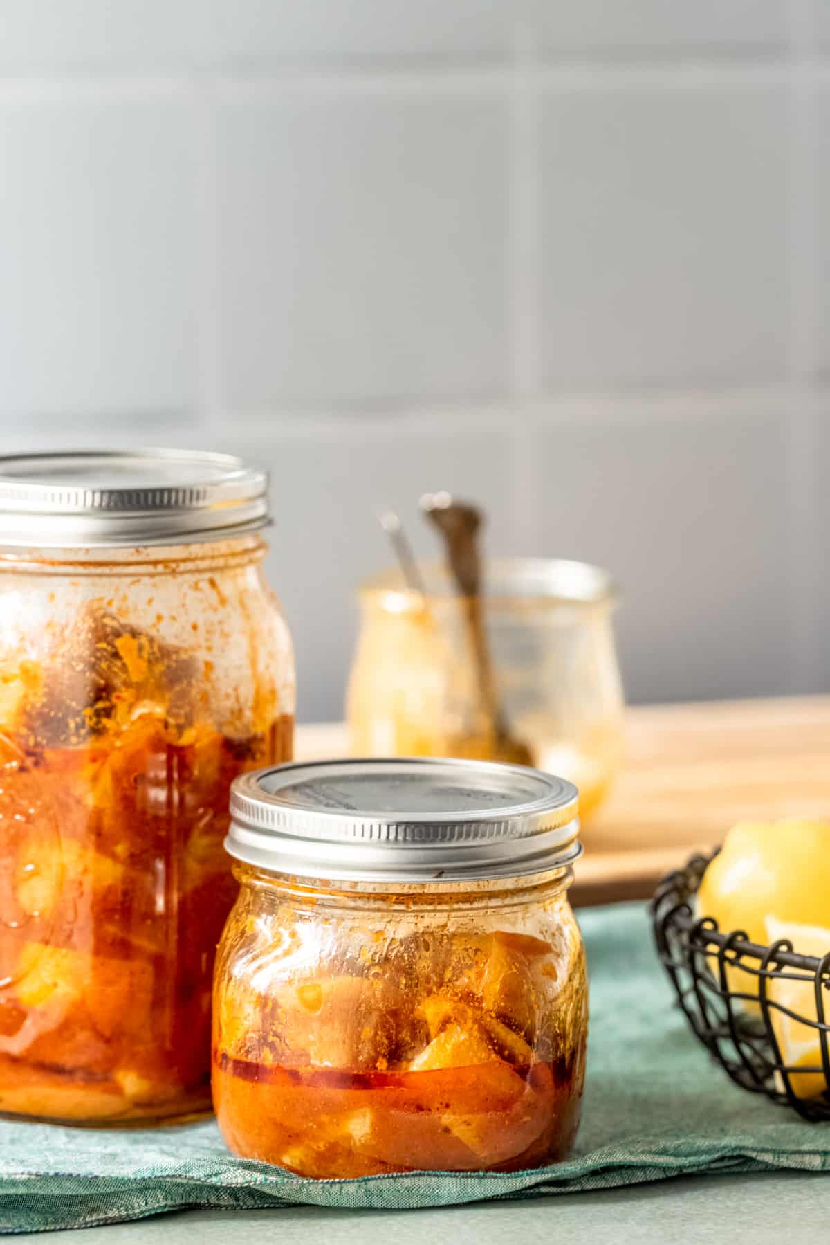 Tangy lemon pickle with whole lemons in golden oil with black mustard seeds in glass container