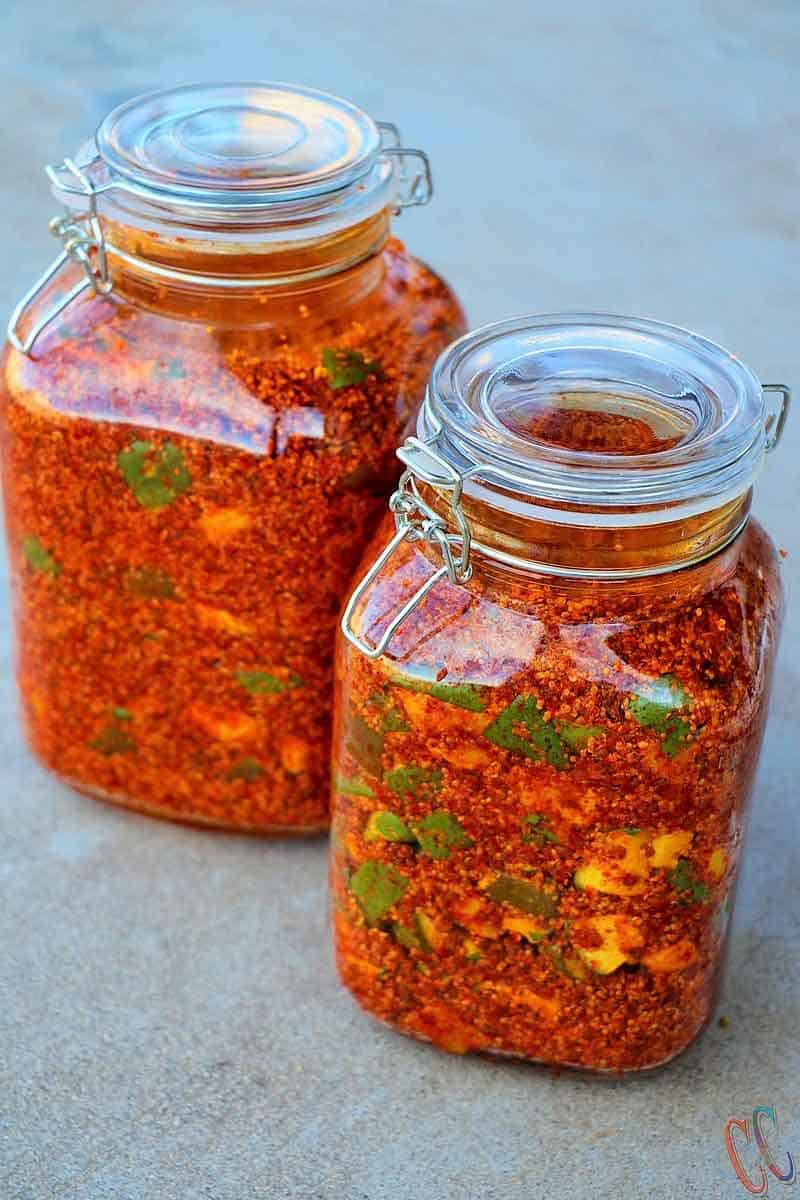 Traditional Indian mango pickle in glass jar with golden oil and red spices on wooden table