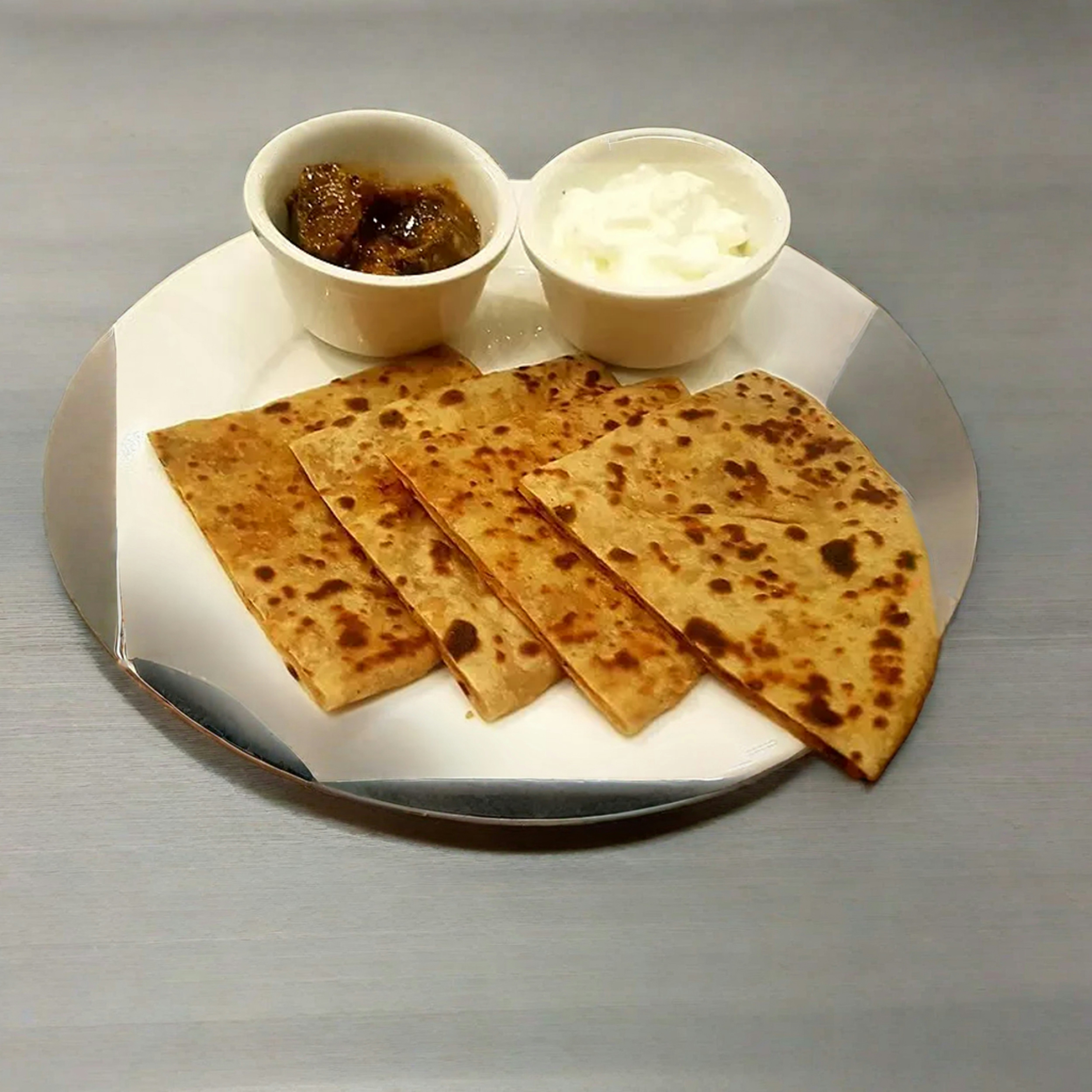Golden crispy paratha stuffed with mango pickle on traditional brass plate with yogurt